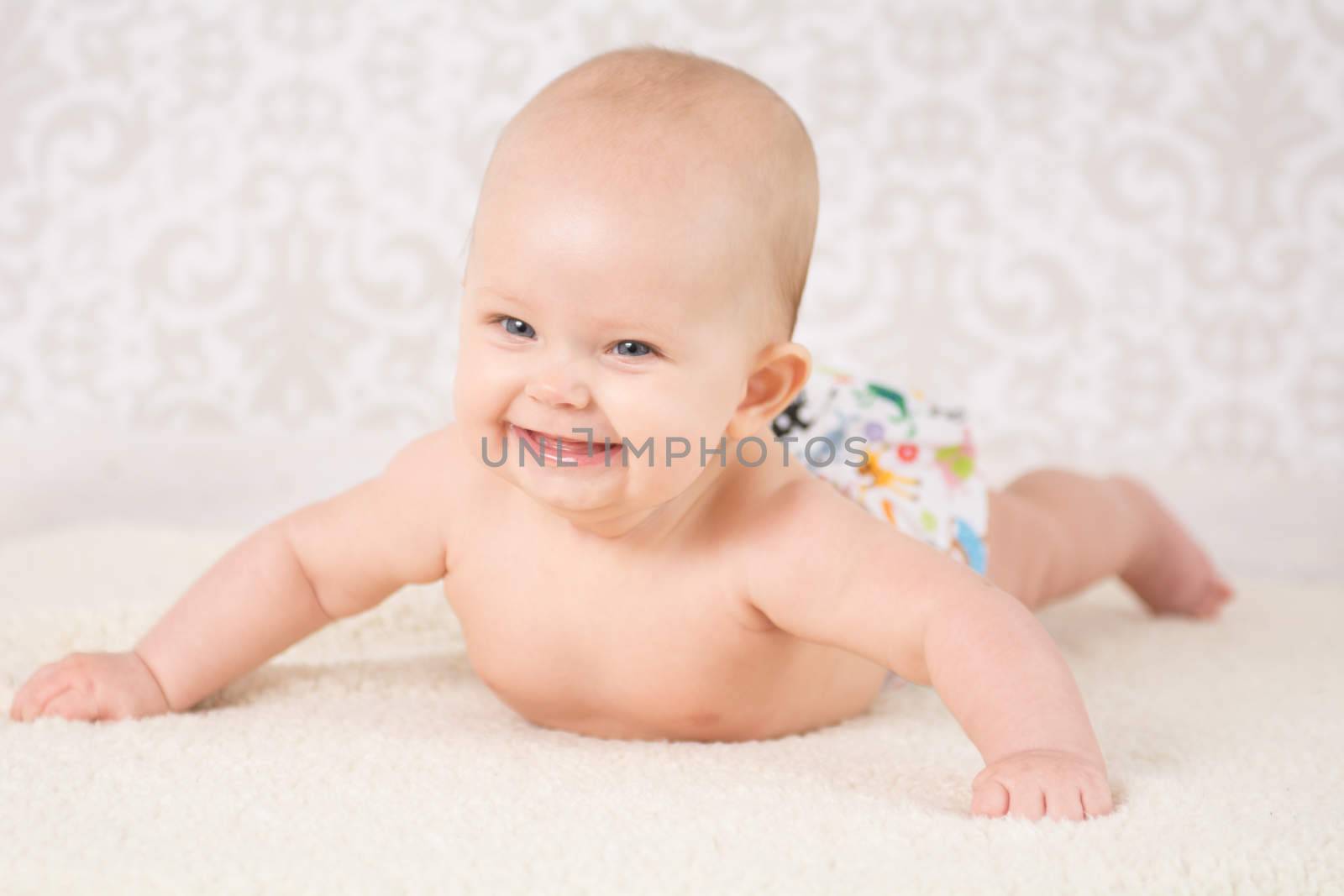 Baby in a reusable nappy, lying on a belly on a light background, arms wide