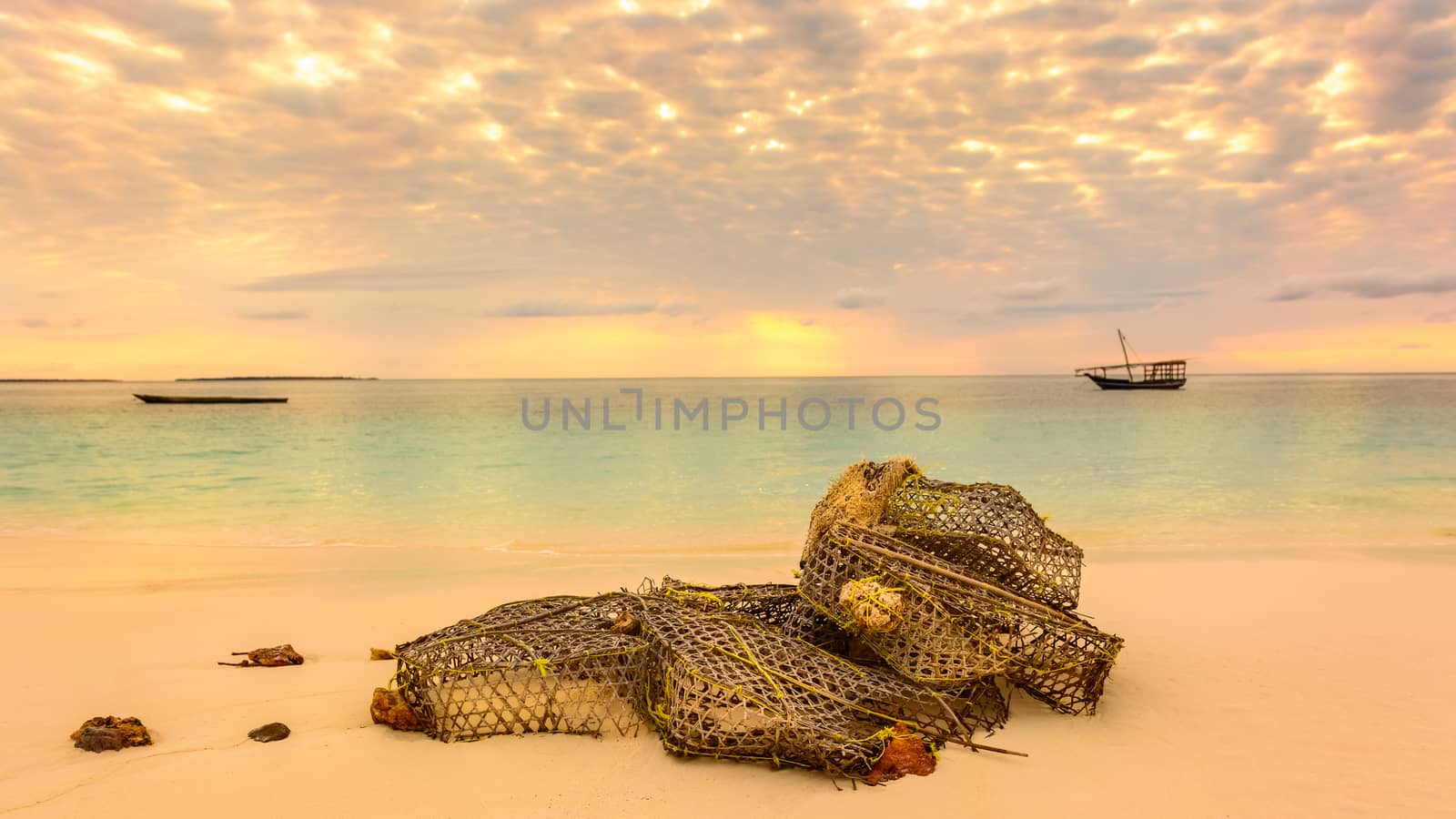 In the beautiful beach of Nungwi (Zanzibar) in the forground a fishing net on the beach,in background two typical local boats (dhows) at sunset.