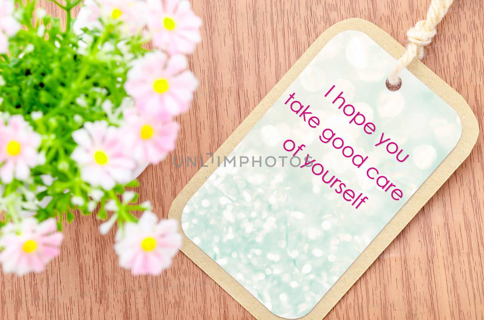 Take care of yourself greeting card with pink flower on wooden background.