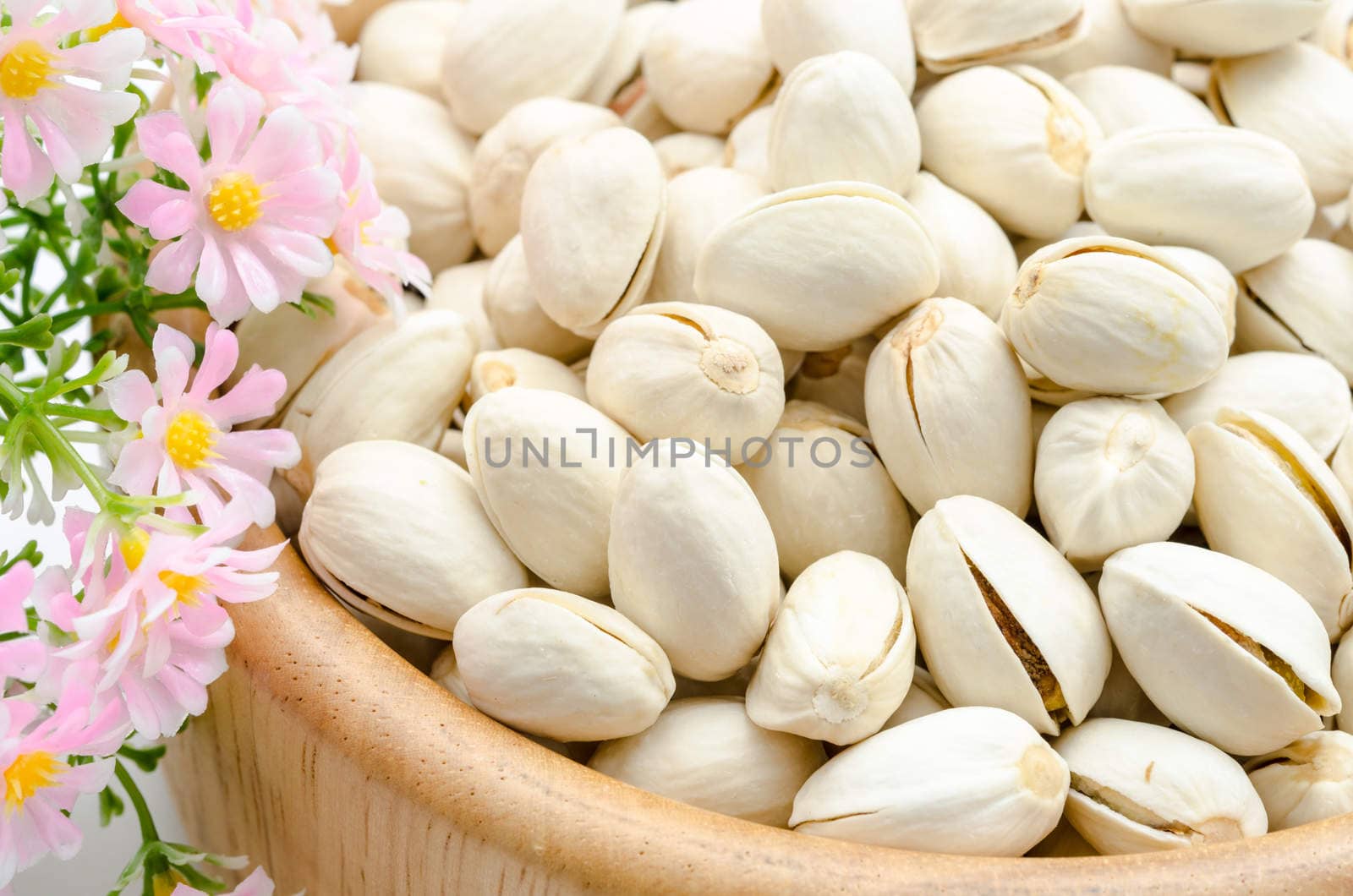 Pistachio nuts in wooden bowl with pink flower.