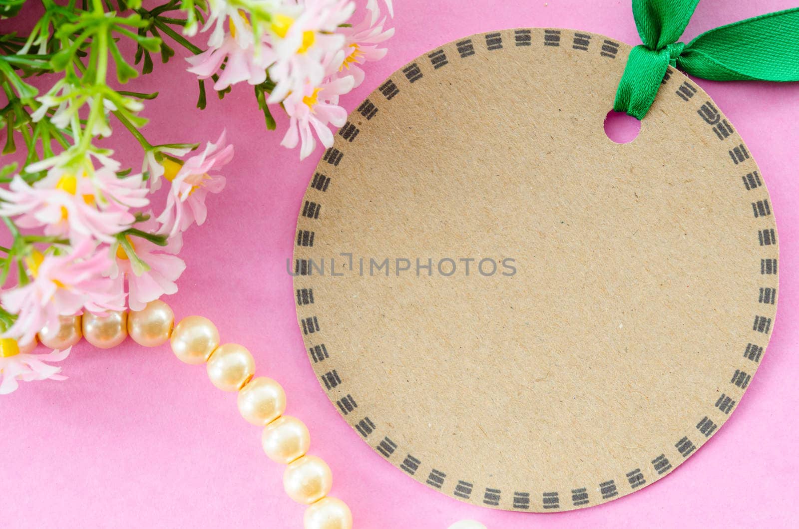 Blank brown tag circle shape and green ribbon with flower on pink background.
