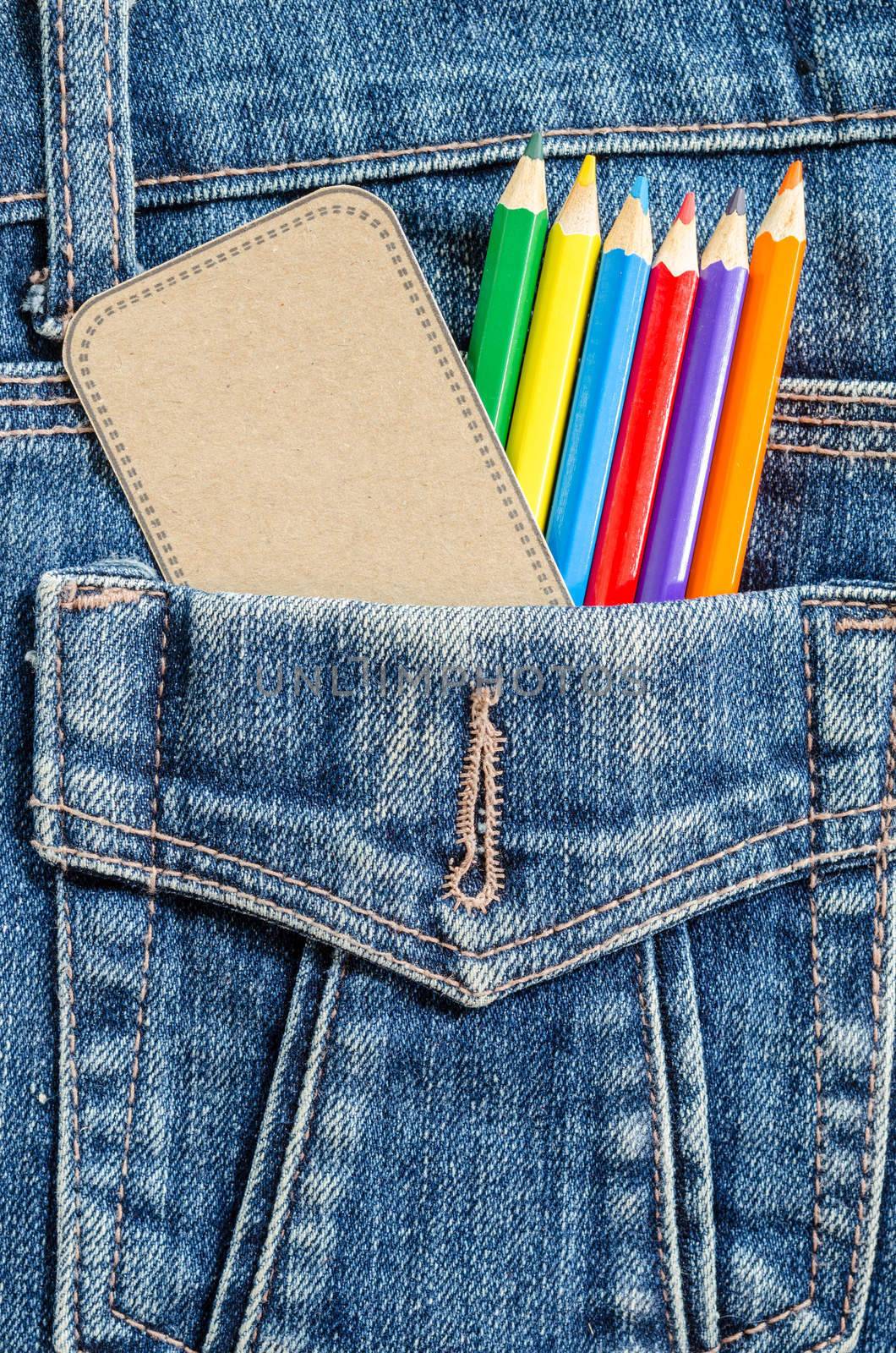 Artist painting concept. Many color pencil and blank brown tag in blue jeans pocket background.