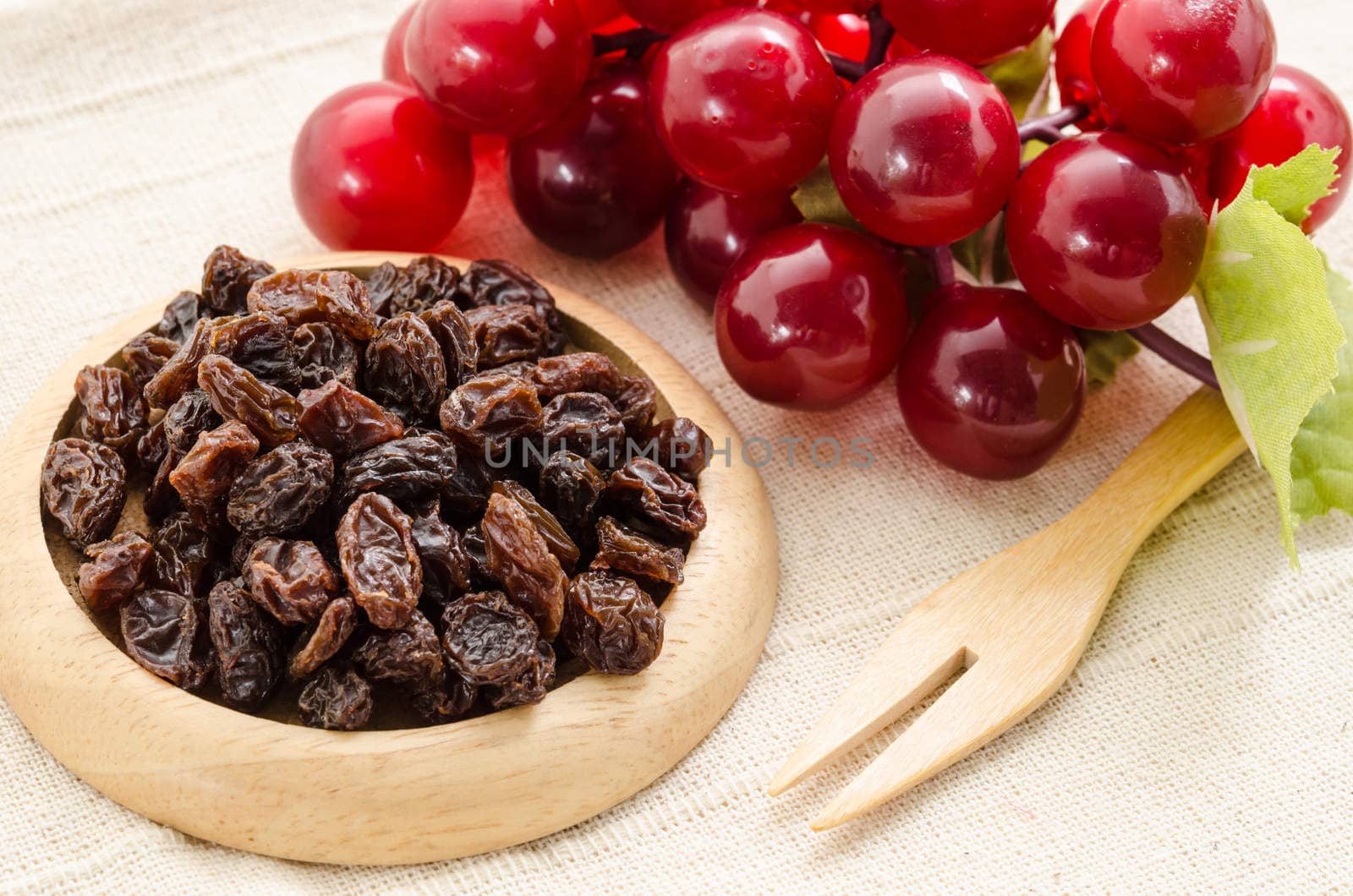 Raisins on a wooden dish and fresh red grapes on fabric background.