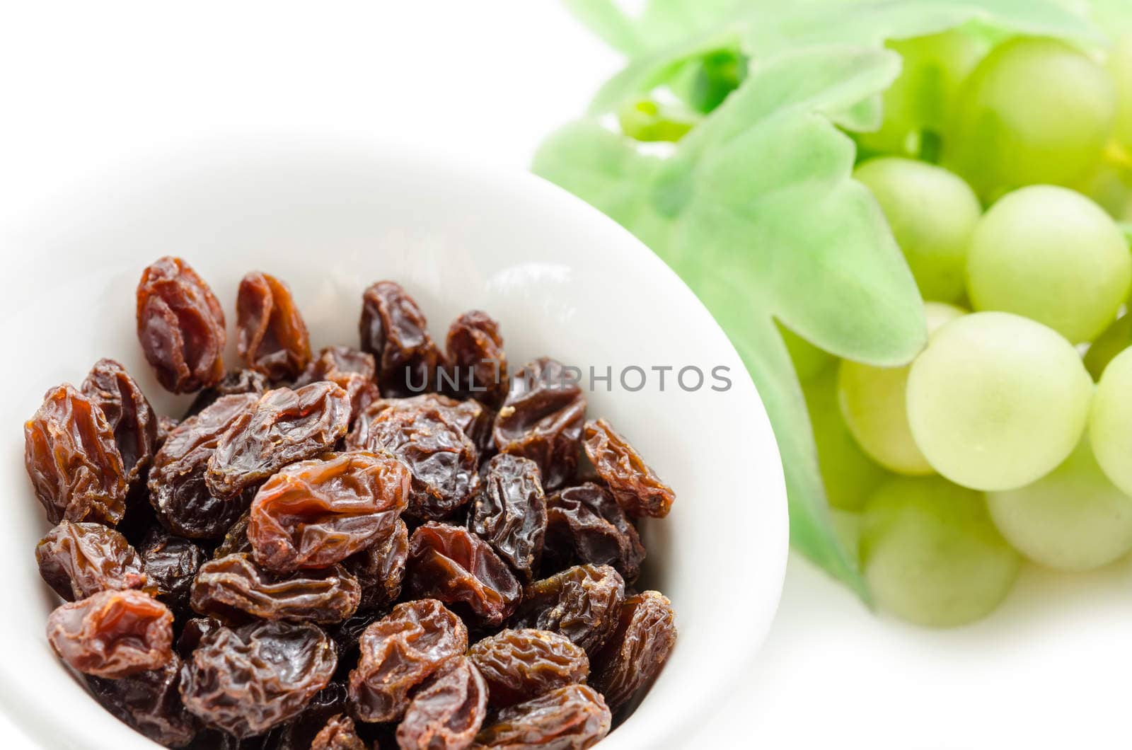 Dried raisins in white cup and fresh grapes on a white background