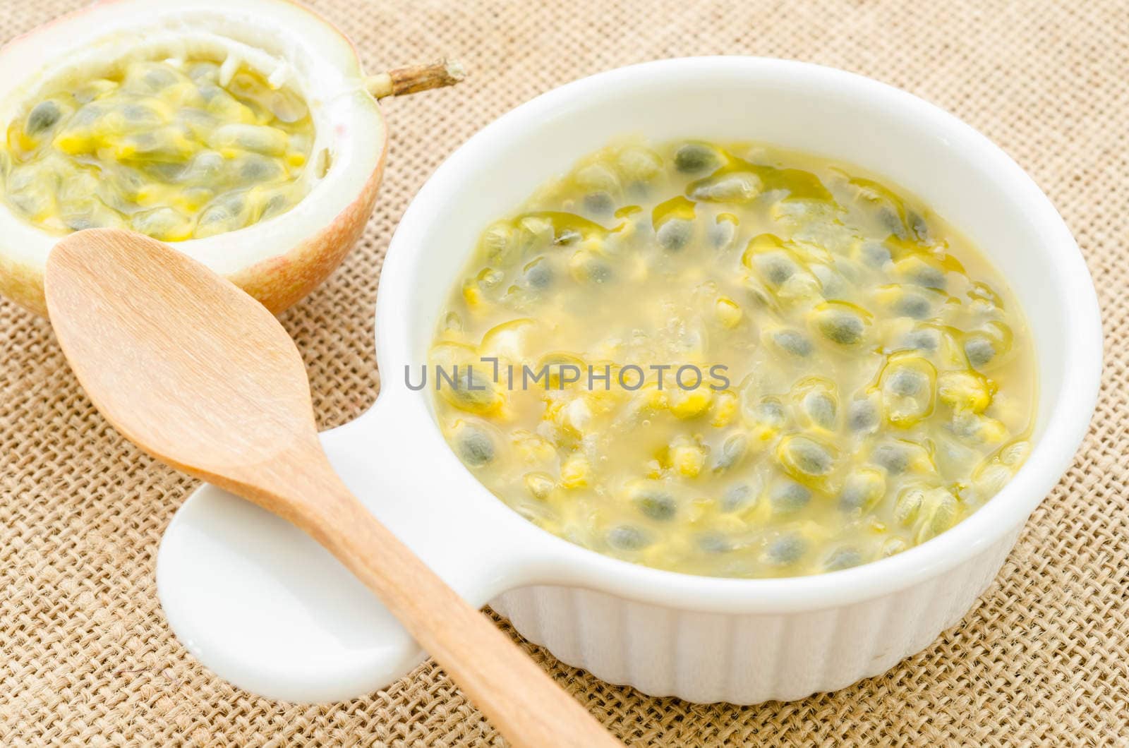 Passion fruit juice in white cup with wooden spoon on sack background.
