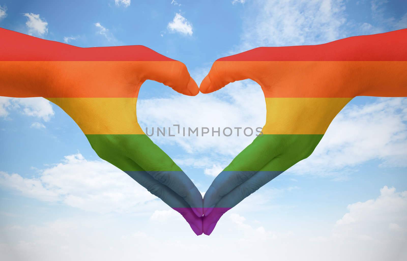 Hands painted as the rainbow flag forming a heart, symbolizing gay love on blue sky. Fredom concept.
