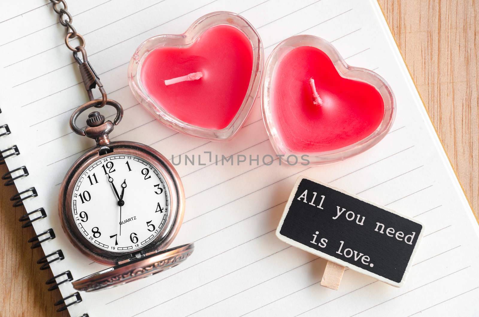 All you need is love. Red heart candle and pocket watch with open diary on wooden background.