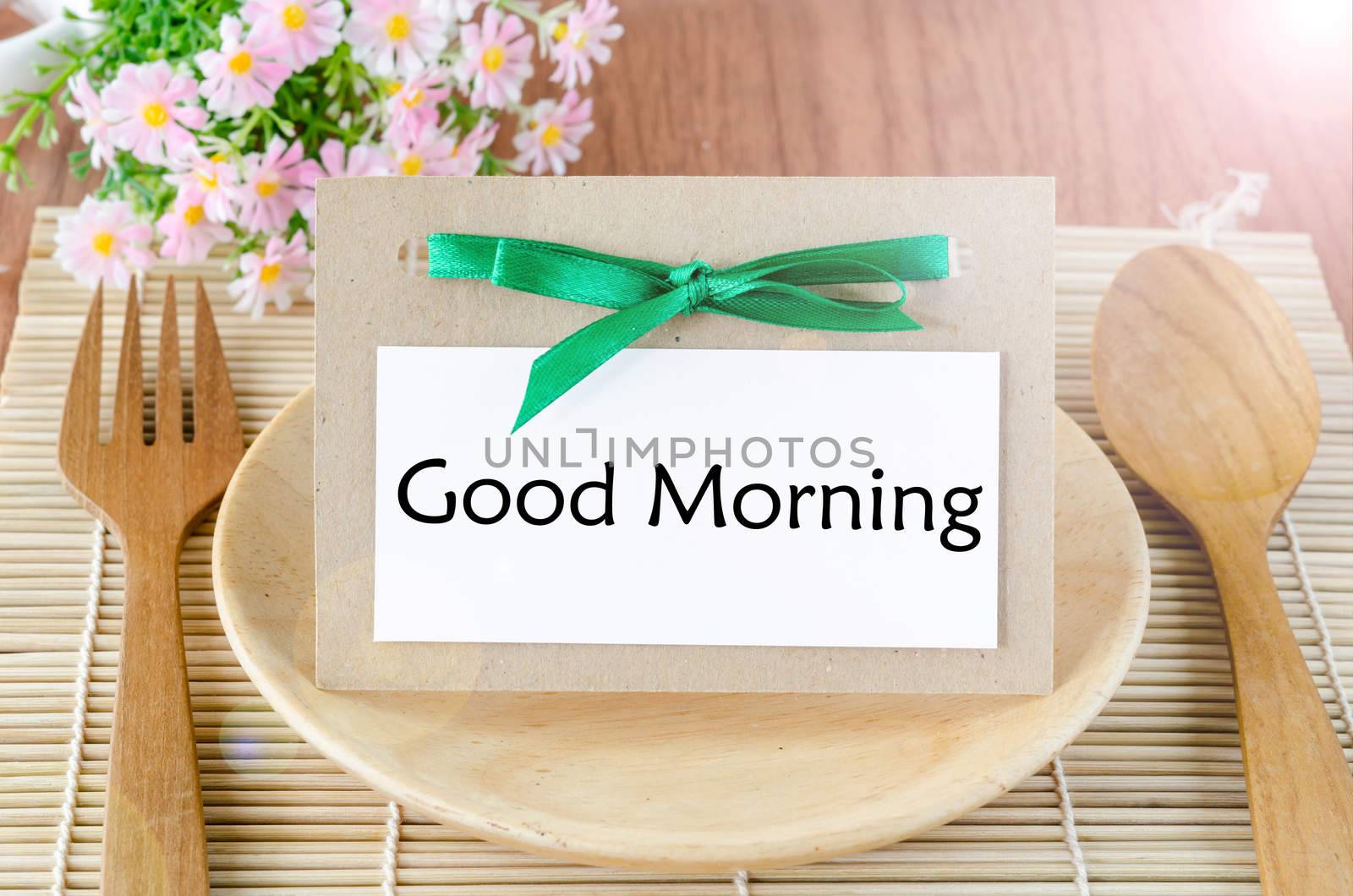 Good morning tag on dish spoon with flower on wooden background.