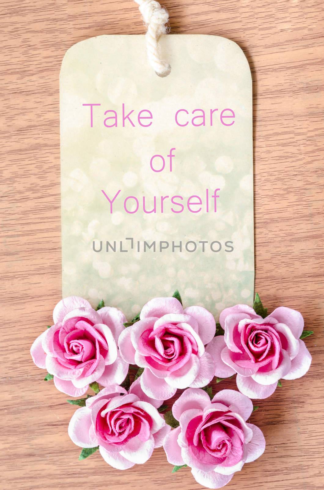 Take care of your self on beautiful tag pink rose on wooden background.