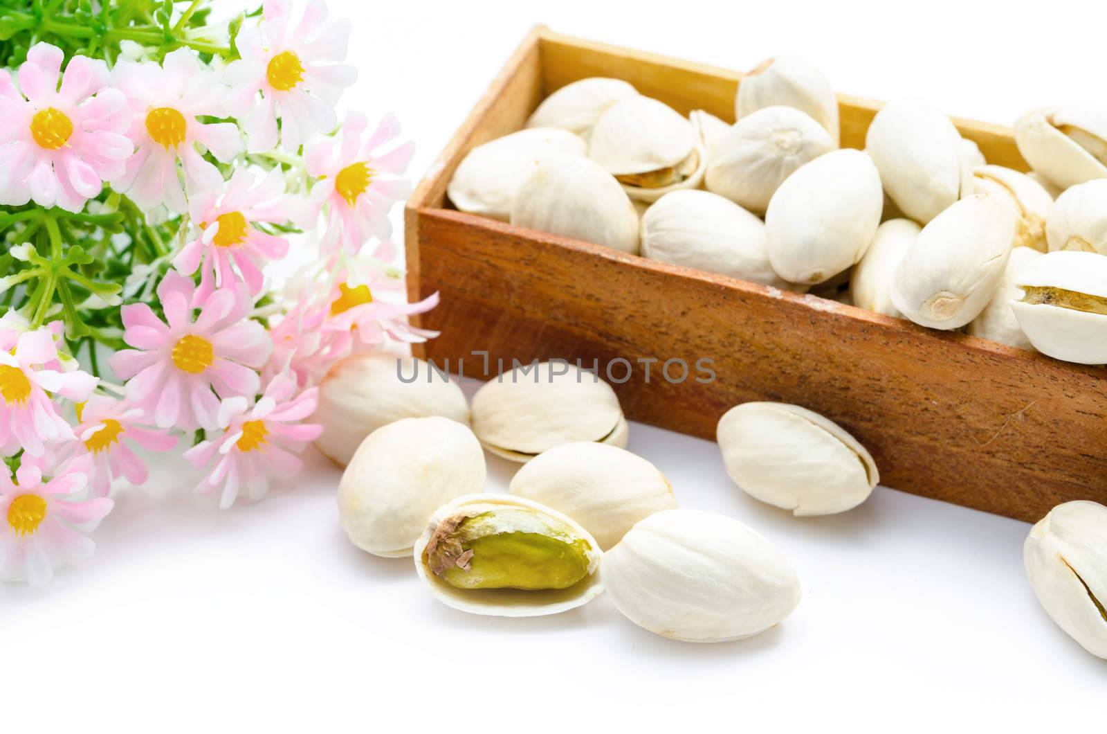 Pistachio nuts in wooden box with flower on a white background.