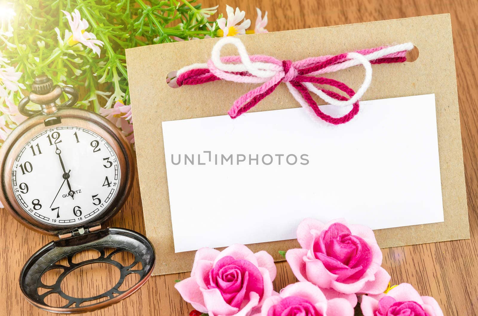 Blank paper tag and pocket watch with pink rose on wooden background.