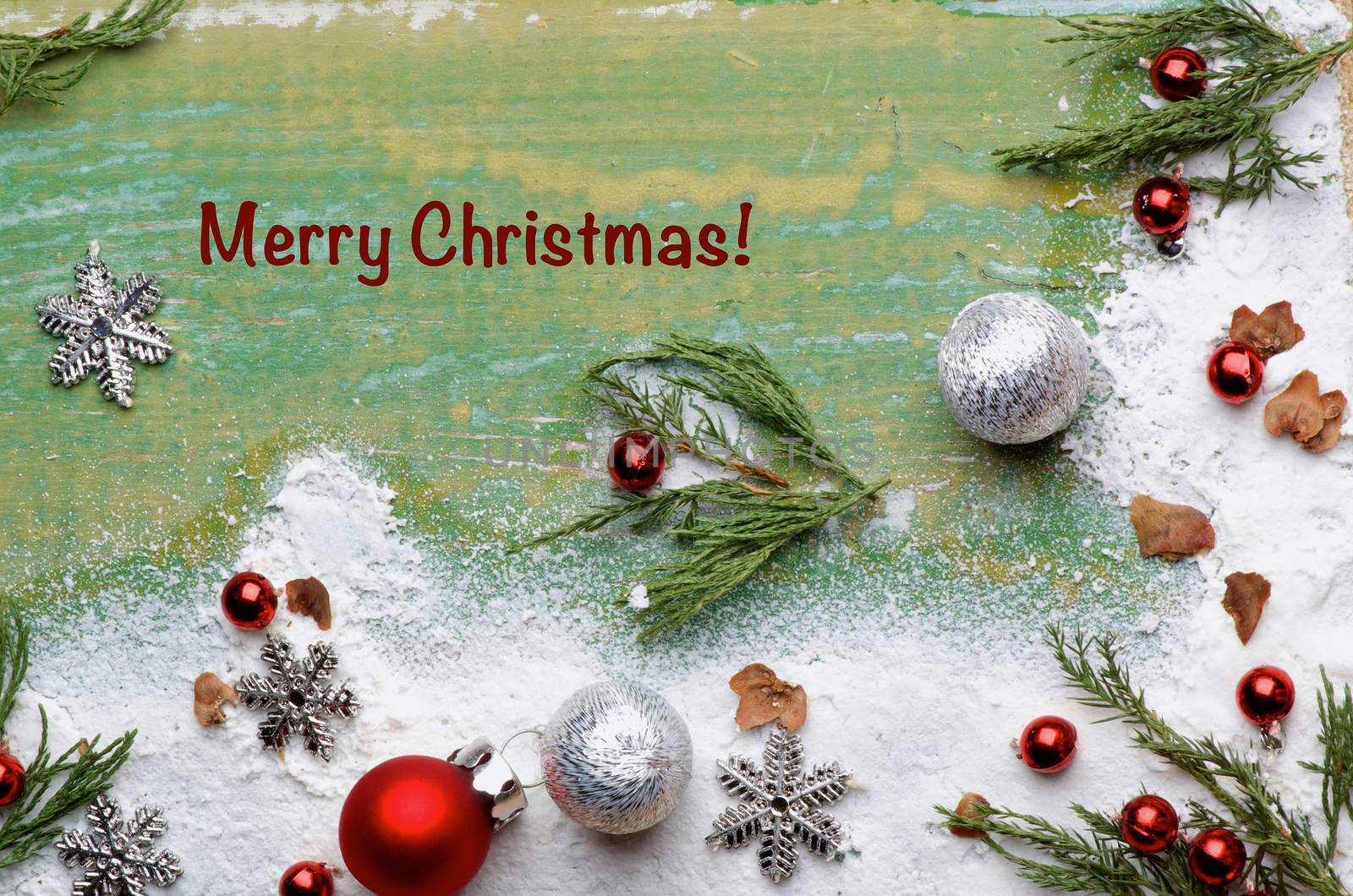 Christmas Greeting Card with Corner Borders of Green Branches, Snow Flakes, Red Baubles and Silver Stars with Inscription closeup on Cracked Wooden background