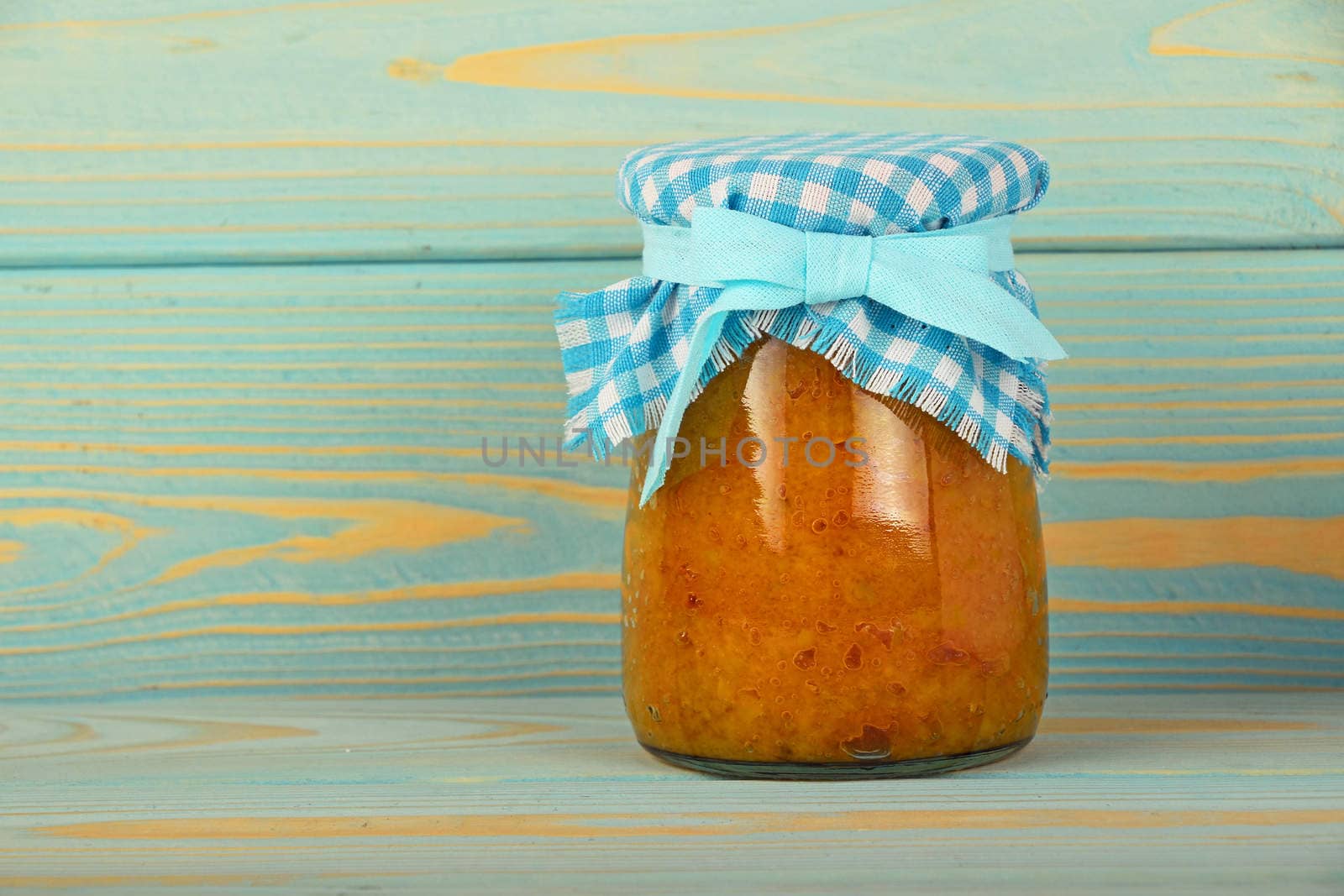 One glass jar of homemade quince jam with textile top decoration at blue painted vintage wooden surface