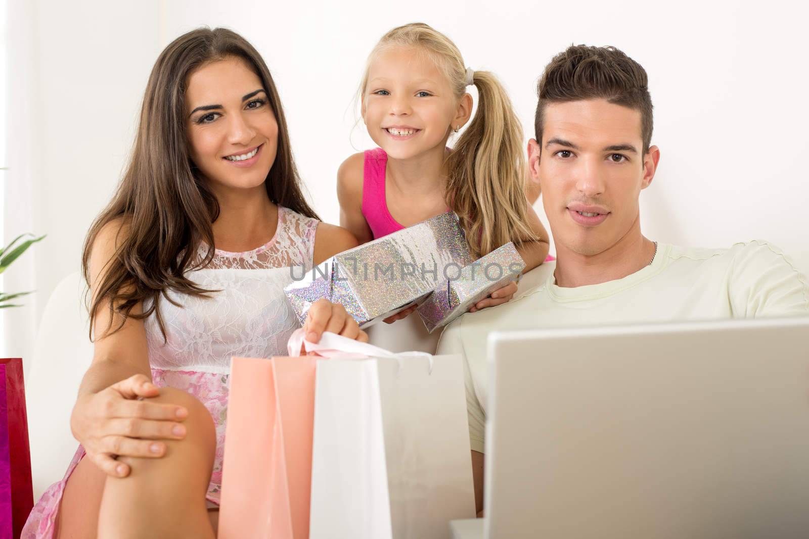 Beautiful happy family sitting at home with laptop and shopping bags. Looking at camera.