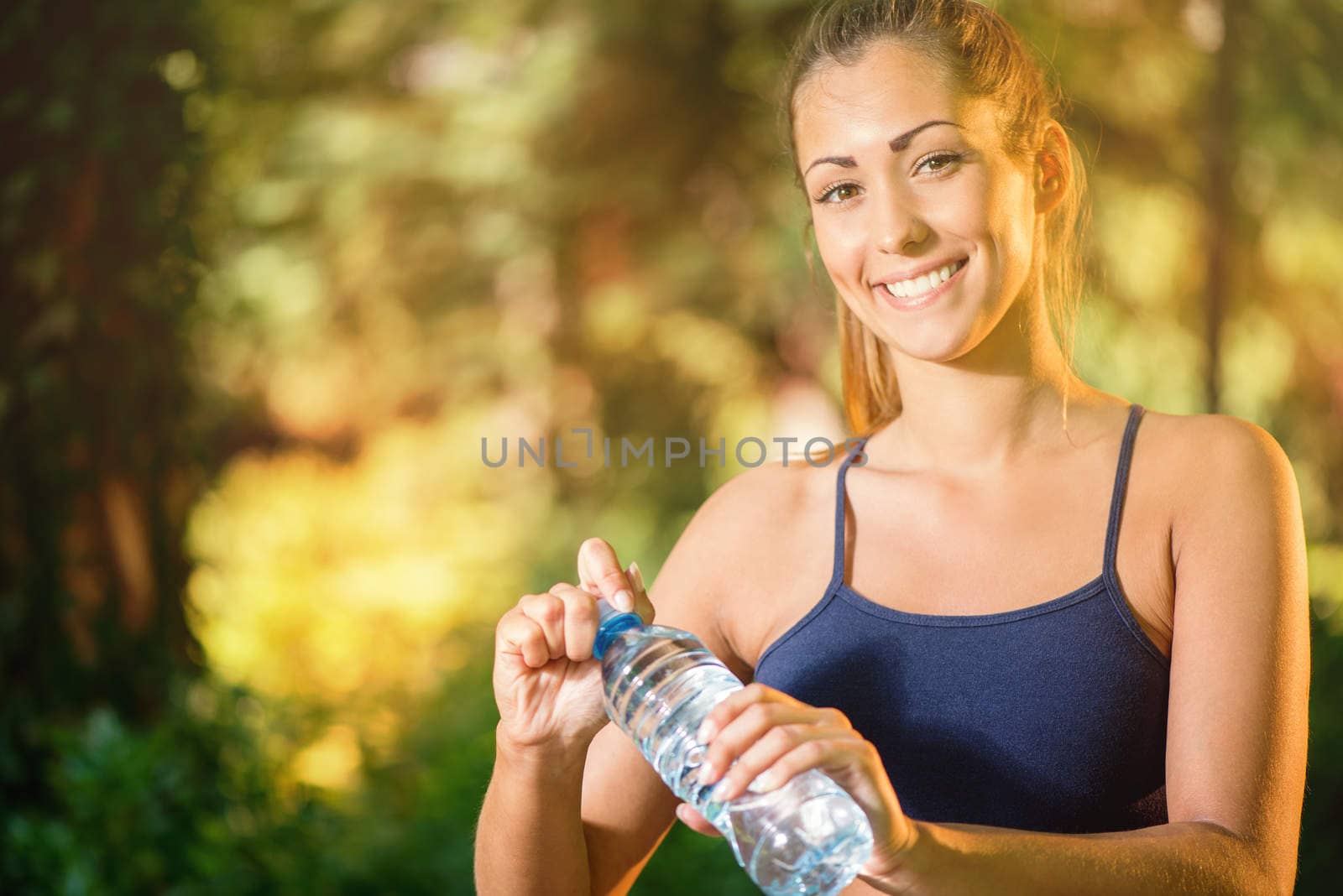 Beautiful young woman holding water bottle after training in the park. Looking at camera. 