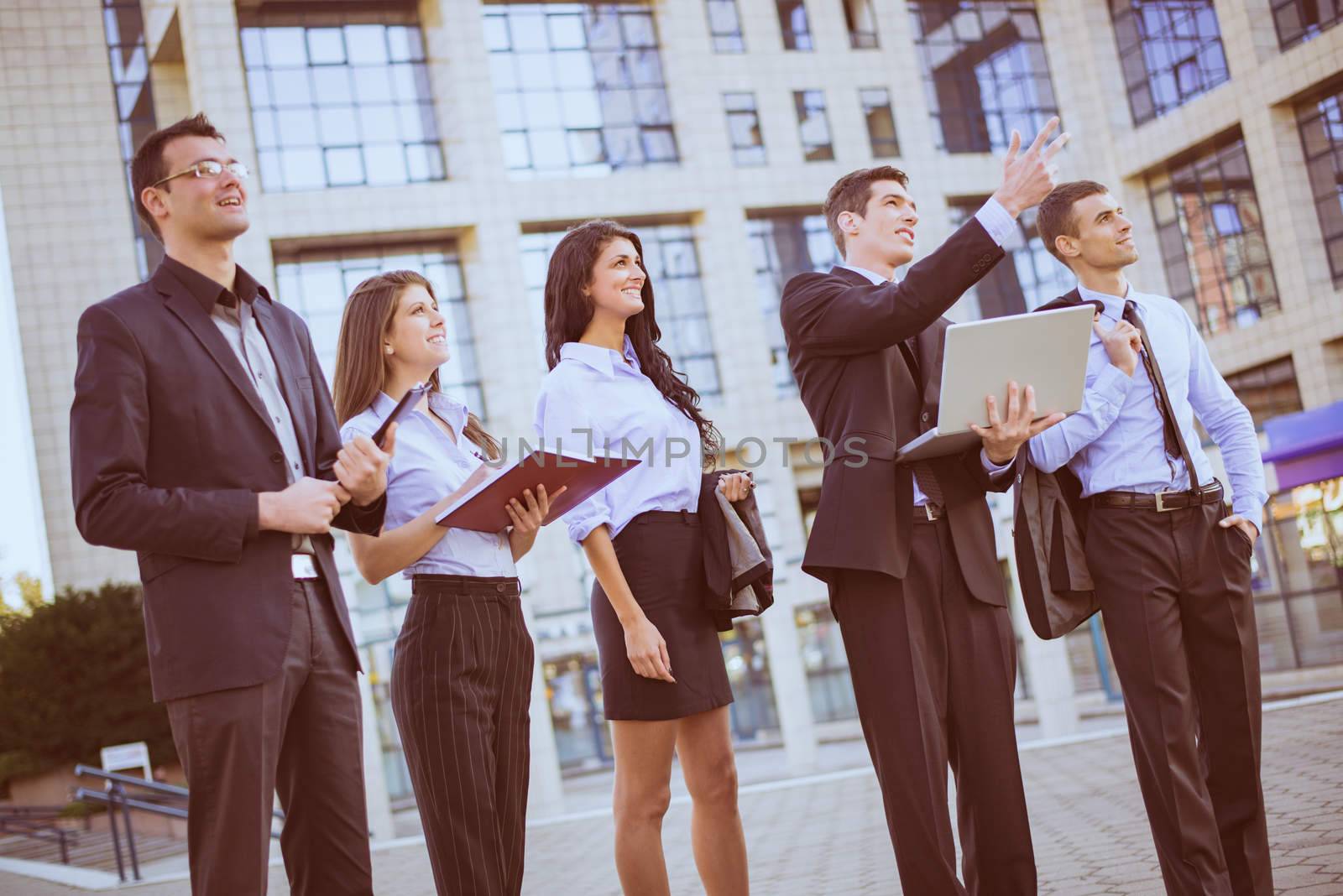 Young businessman with laptop in front of office building outstretched fingers of the hand, aimed at heights, explaining his colleagues business plan.