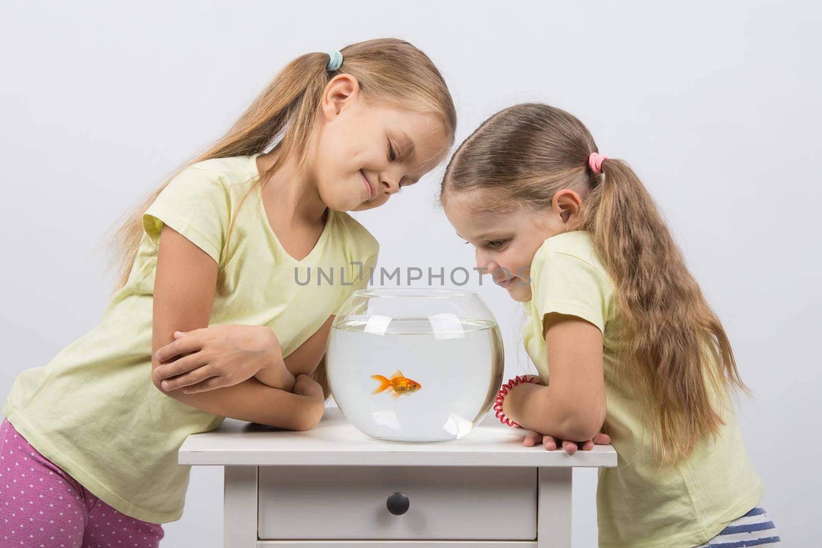 Two happy girls four and six years are at the table on which stands a fishbowl with goldfish