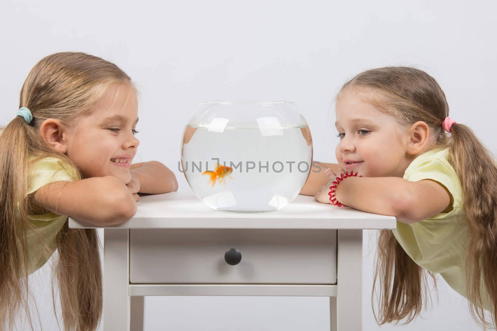 Two happy girls four and six years are at the table on which stands a fishbowl with goldfish