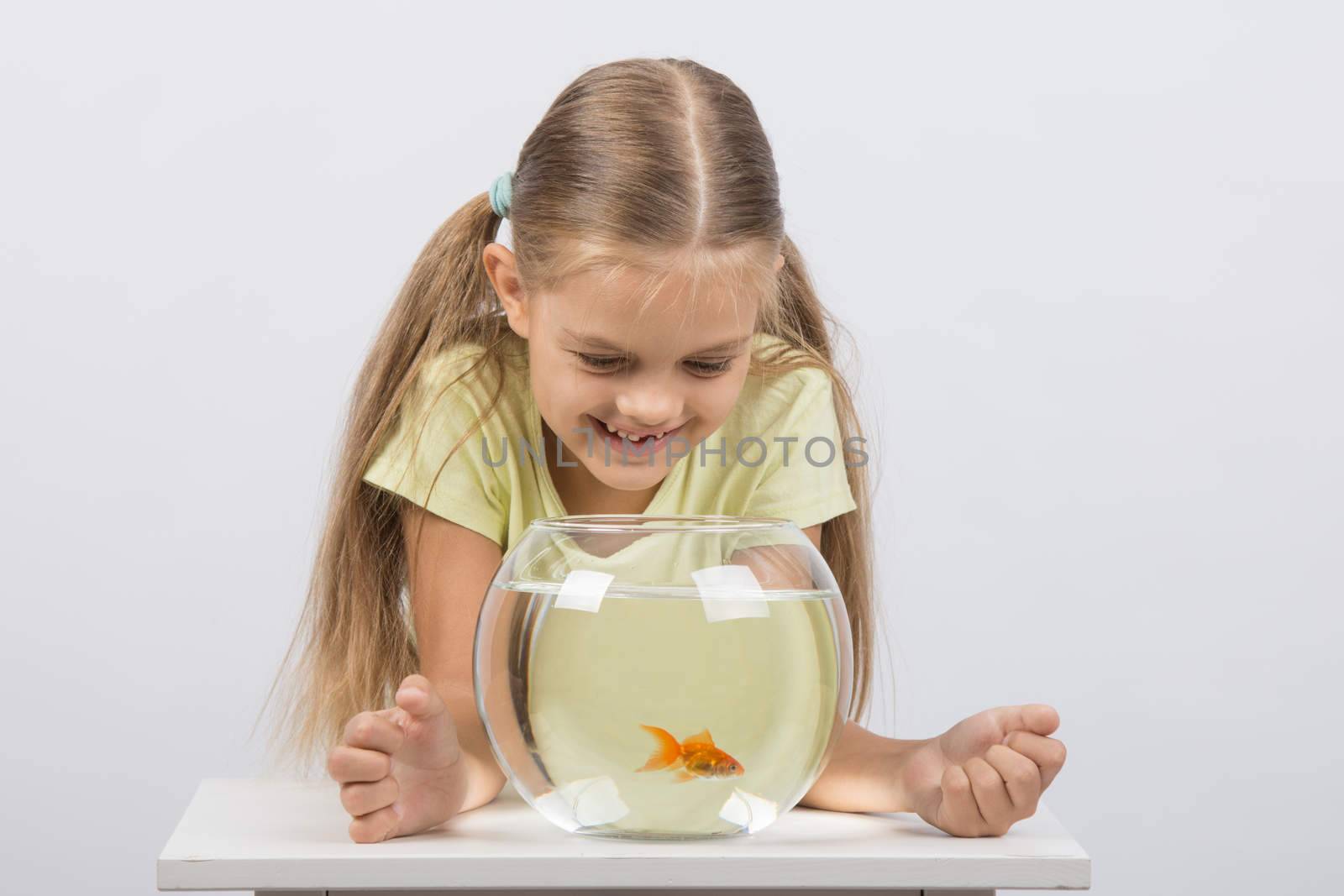 Happy six year old girl sits at a table at the fishbowl with goldfish