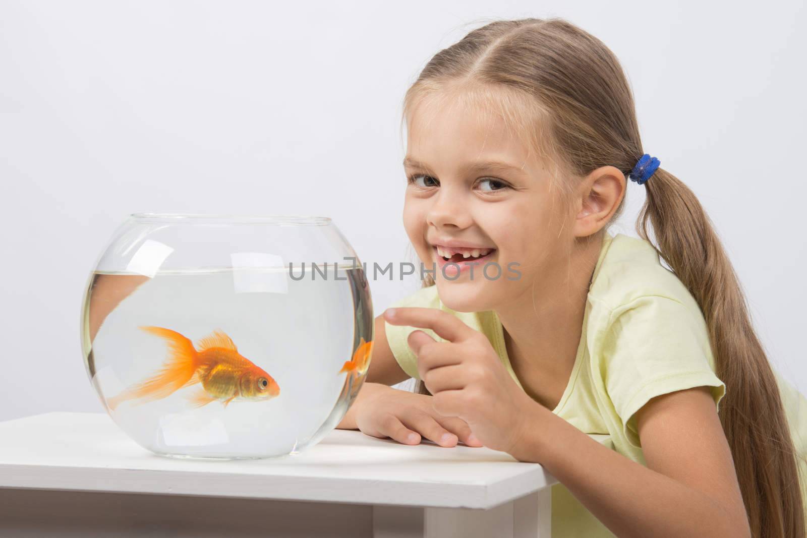 Happy six year old girl sits at a table at the fishbowl with goldfish
