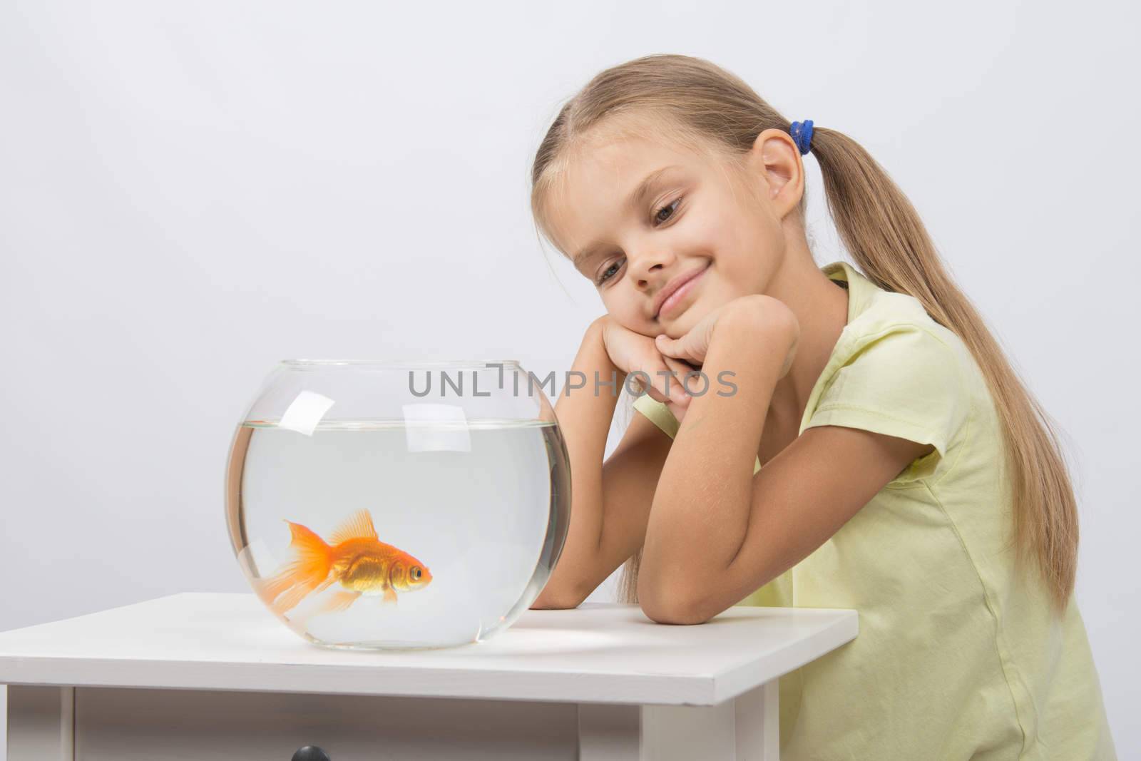 Happy six year old girl sits at a table at the fishbowl with goldfish