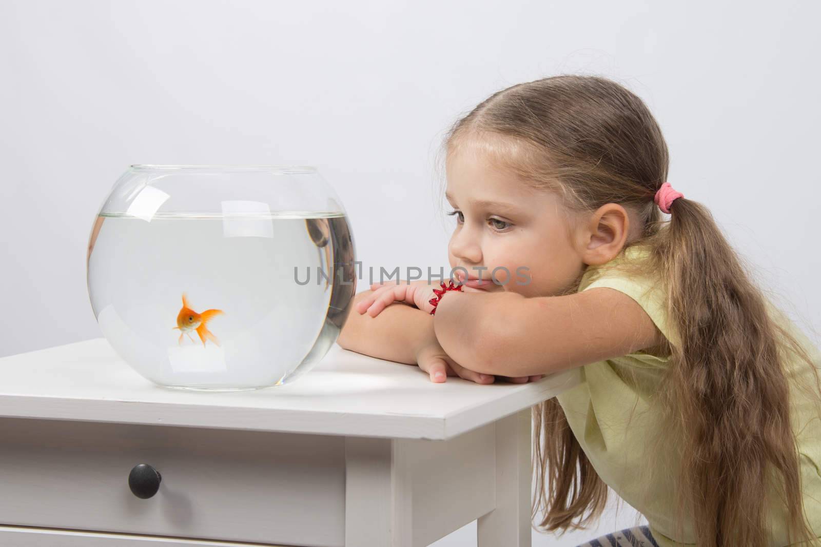 happy four-year girl sitting at a table near fishbowl with goldfish