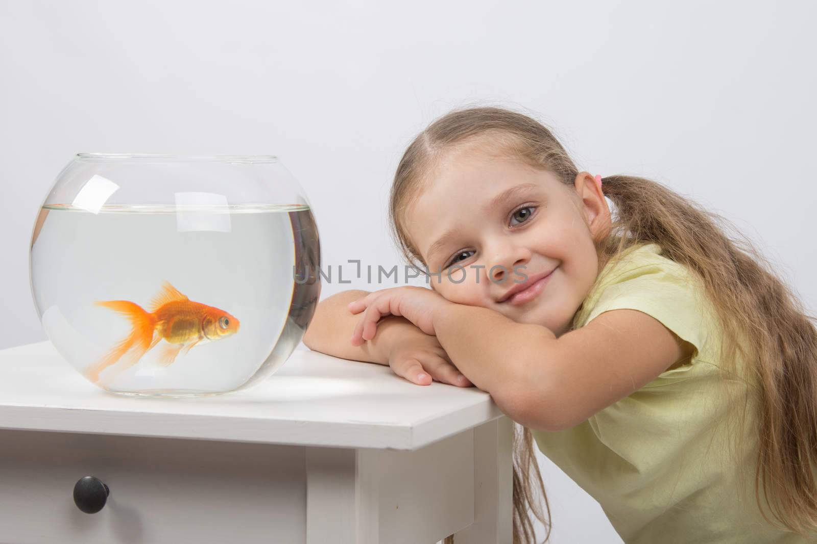happy four-year girl sitting at a table near fishbowl with goldfish