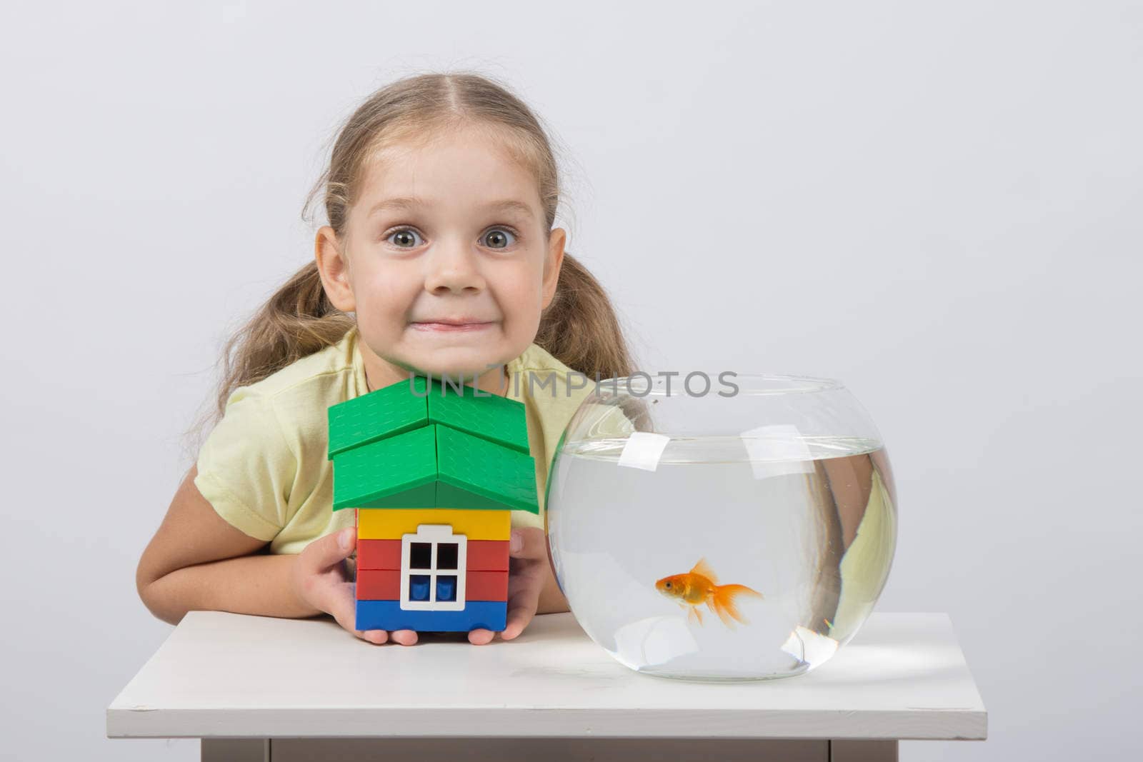 happy four-year girl sitting at a table near fishbowl with goldfish