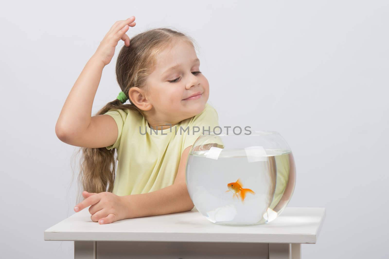 happy four-year girl sitting at a table near fishbowl with goldfish