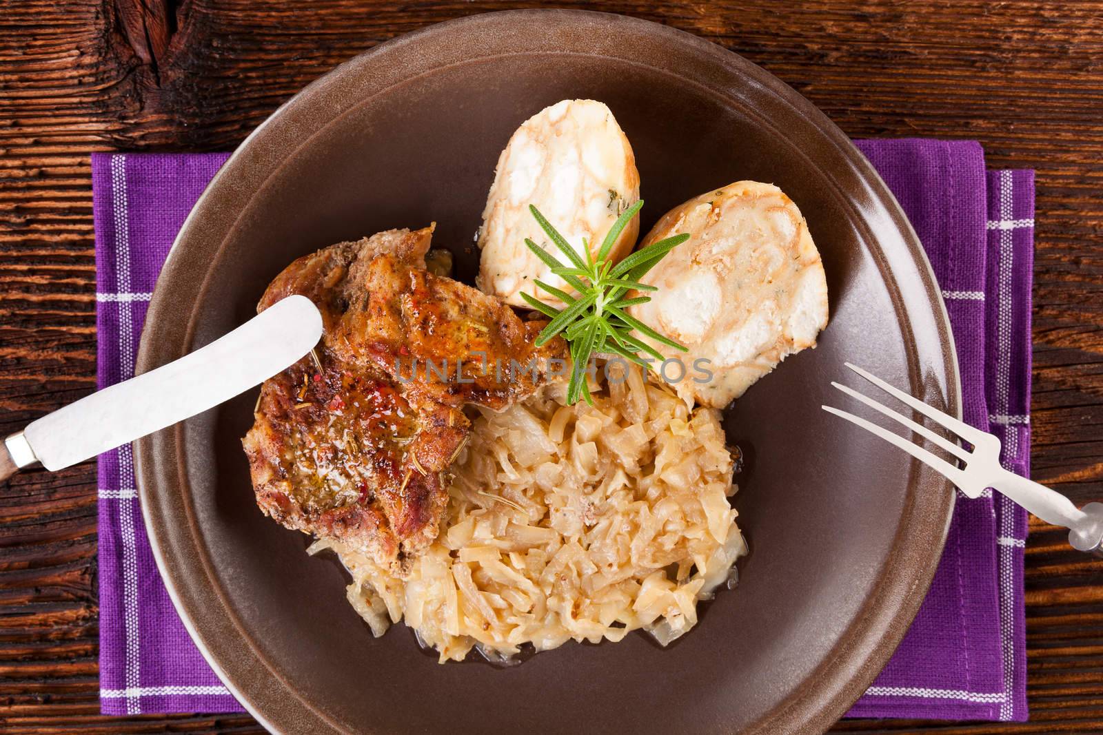 Baked pork chop with dumplings and sauerkraut on plate with silver cutlery on wooden table, top view. 