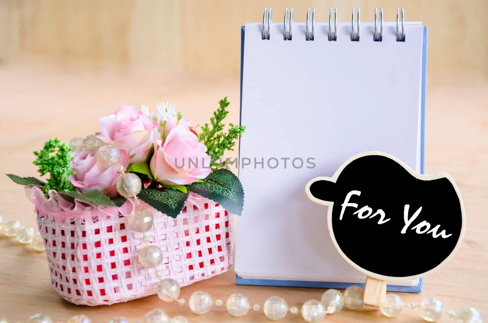 For you wording in black tag and open blank diary with flowers on wooden background.