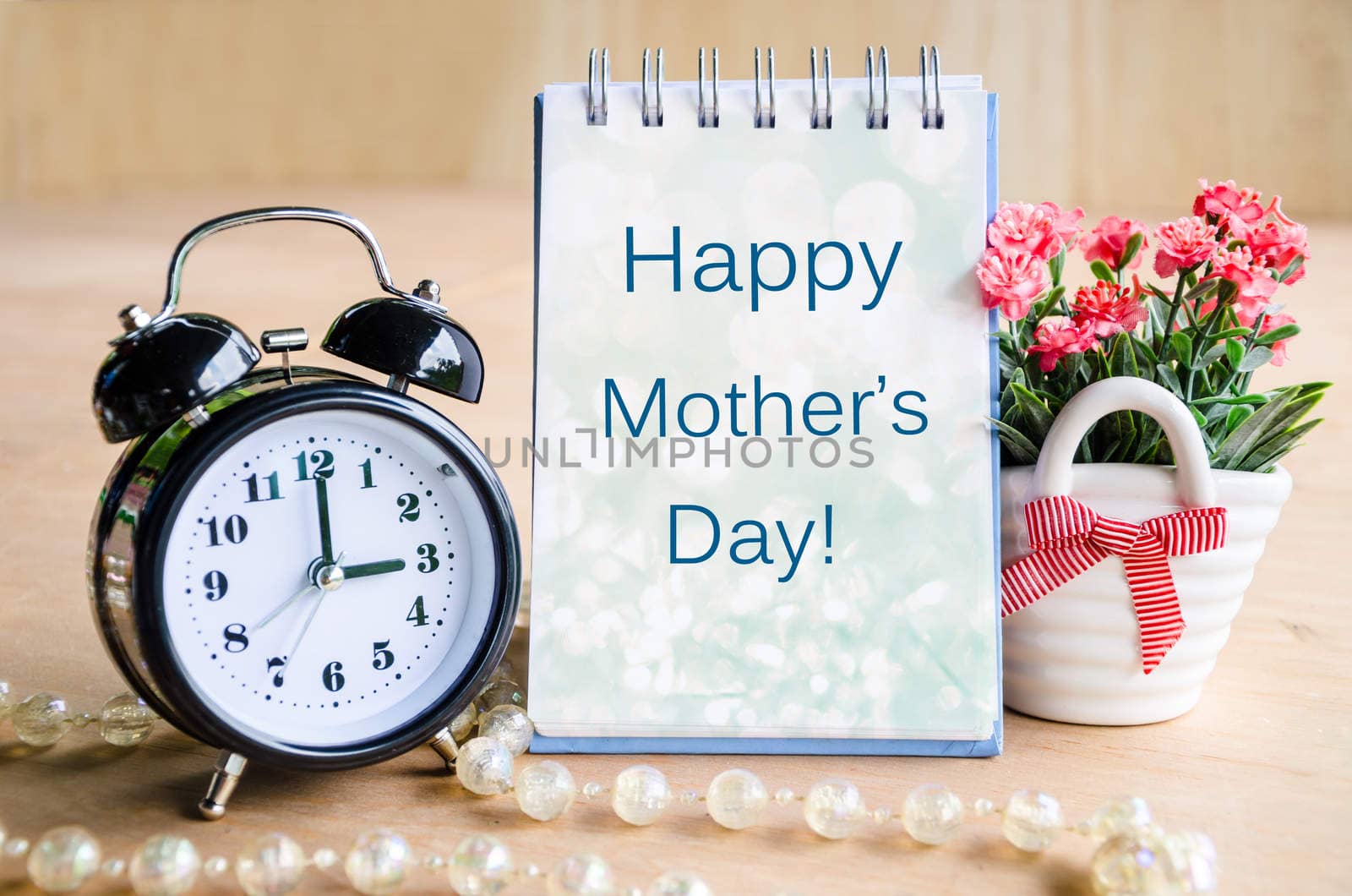 Mothers day card and alarm clock with flowers on wooden background.