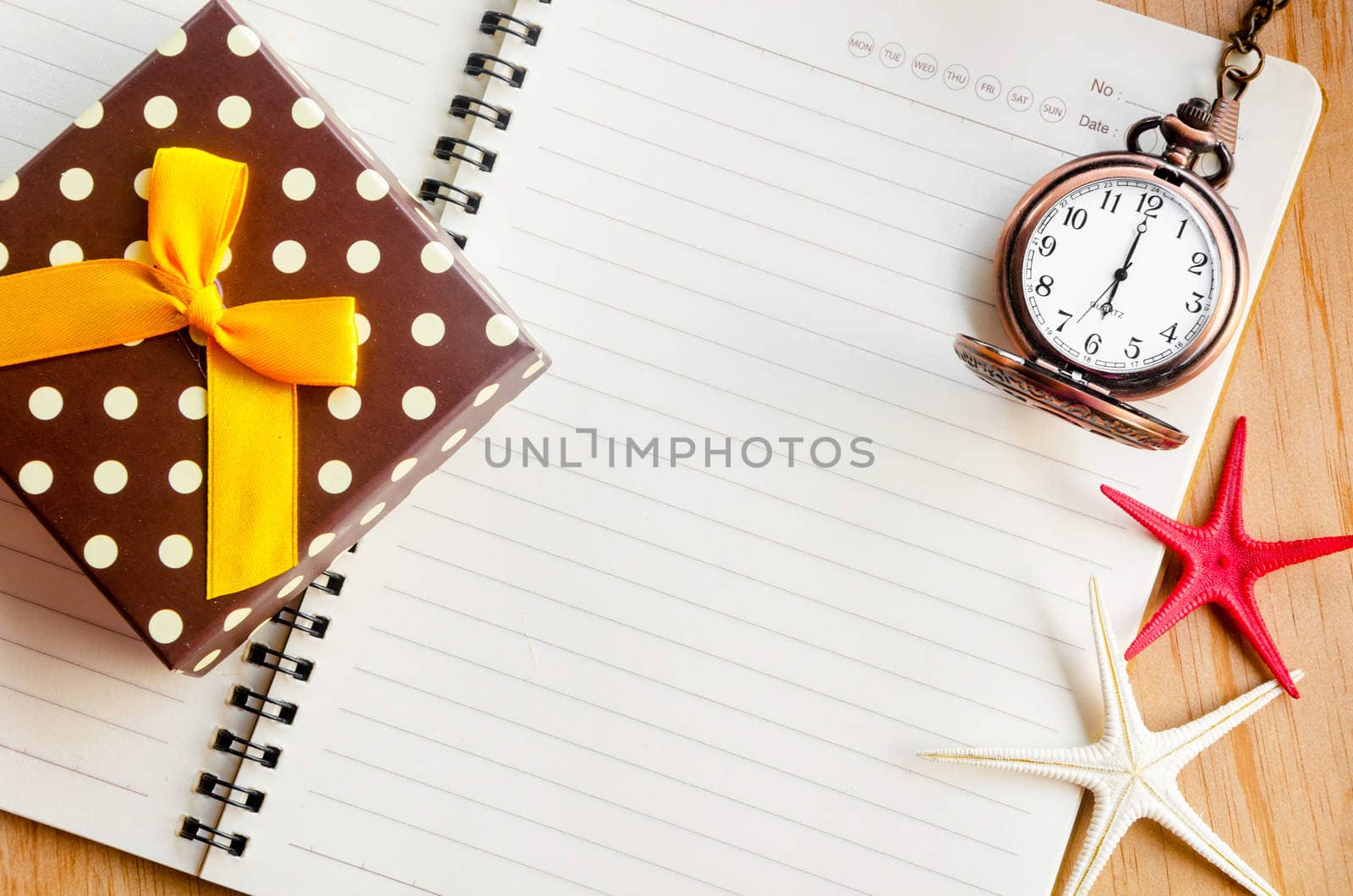 Open diary and pocket watch with gift box on wooden background.