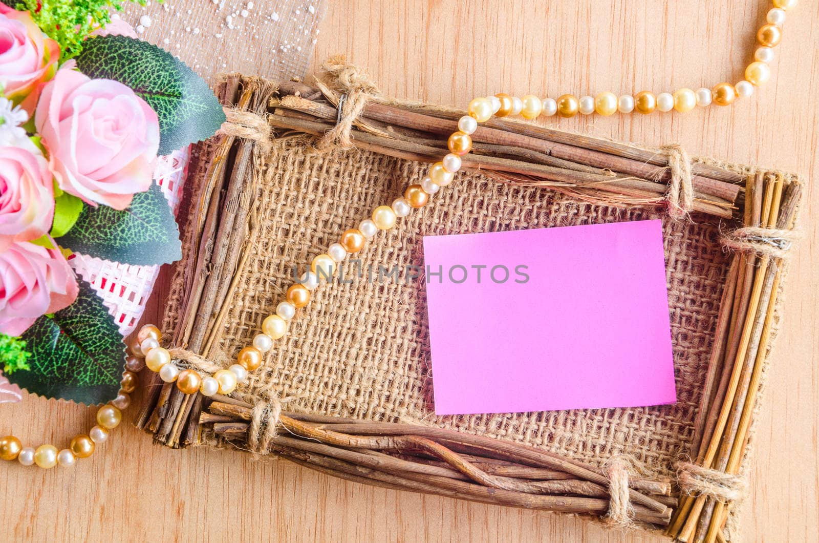 Blank pink note and flower with sack frame on wooden background.