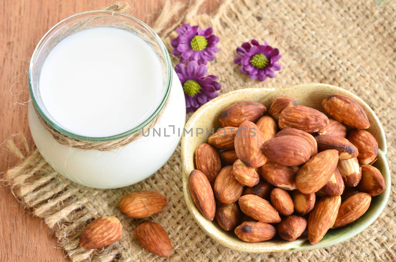 Glass of almond milk with almonds on wooden background.