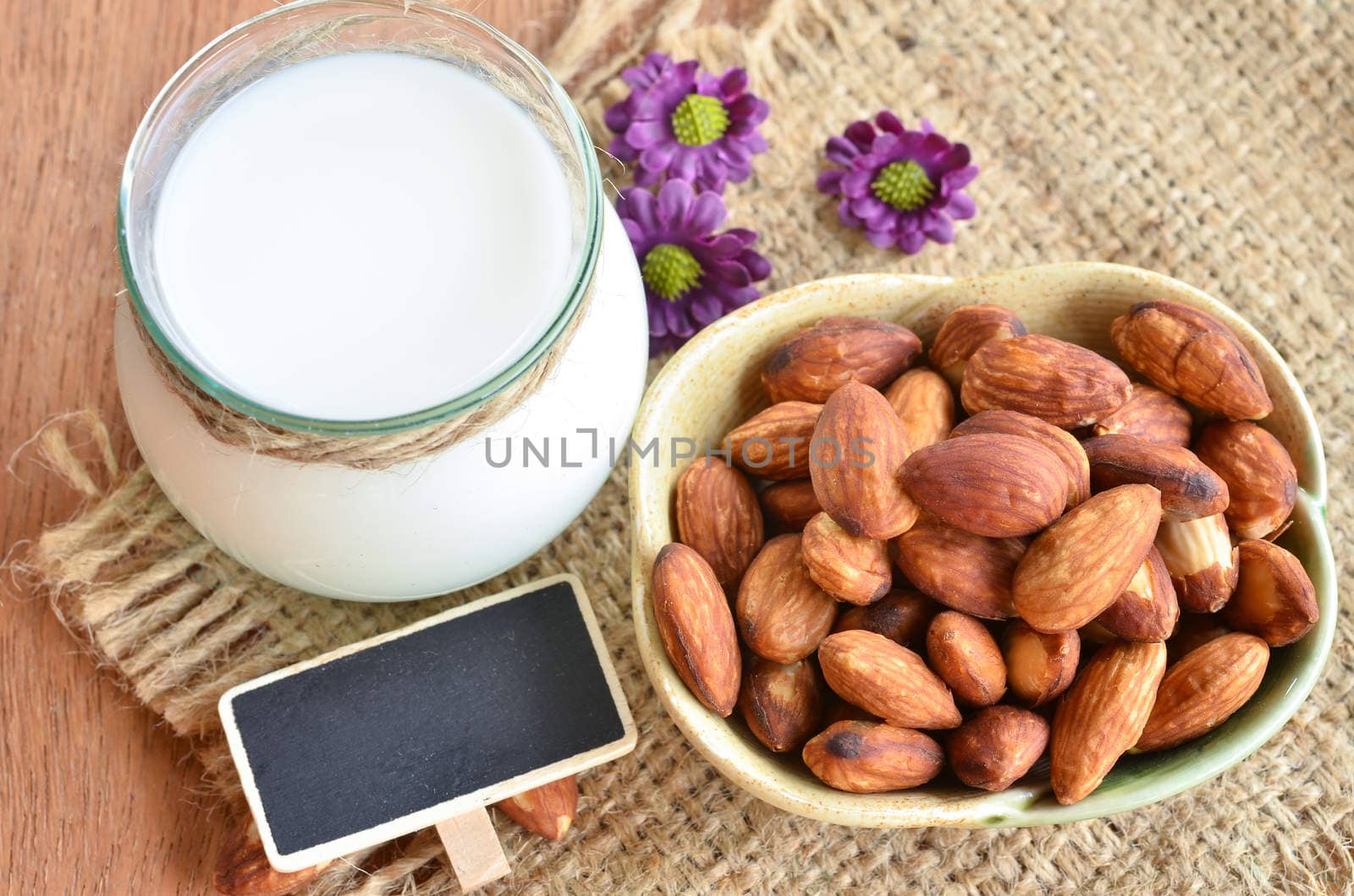 Almond milk in glass with almonds and blank tag on sack background.