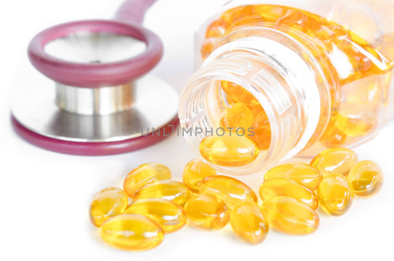 Fish oil capsules spilling out of a bottle and stethoscope on white background.