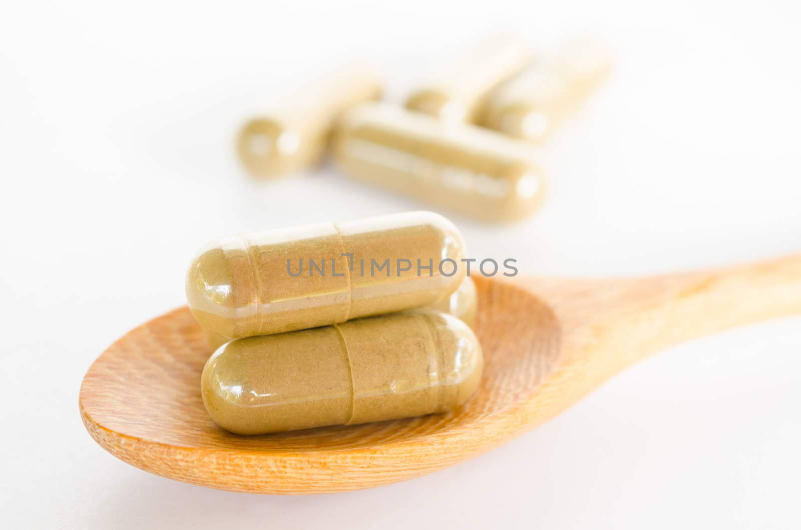 herbal drug capsule on wooden spoon on white background.