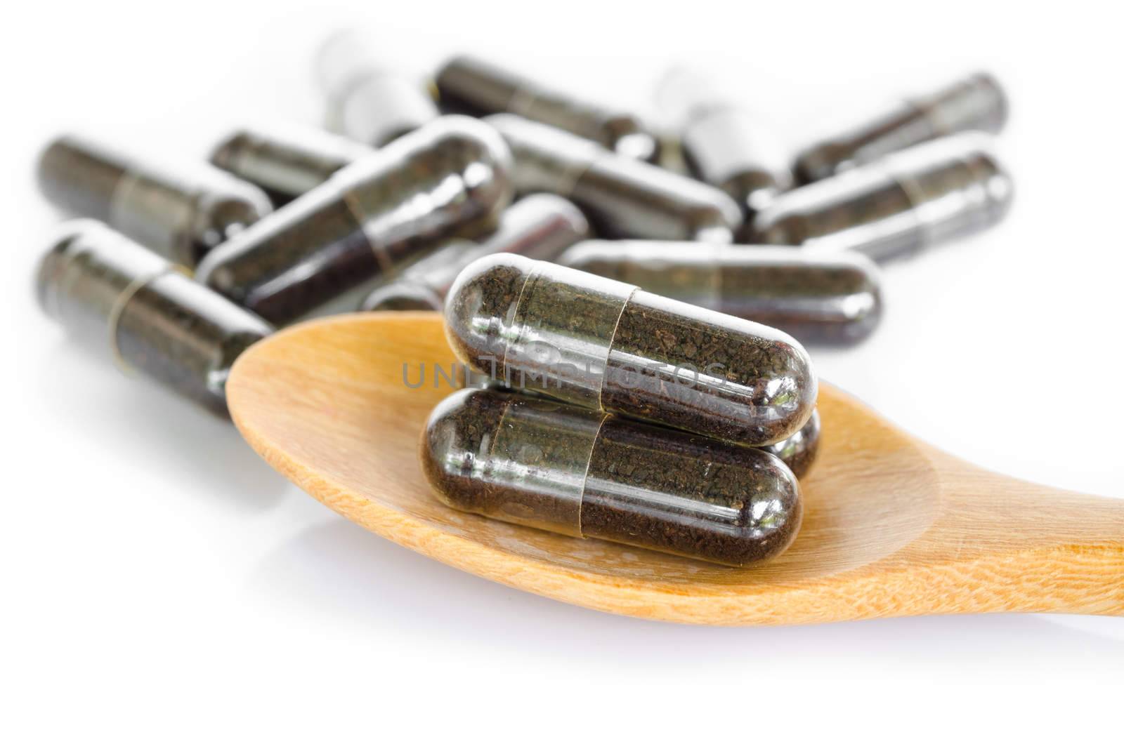 Black herbal capsule drug in wooden spoon on white background.