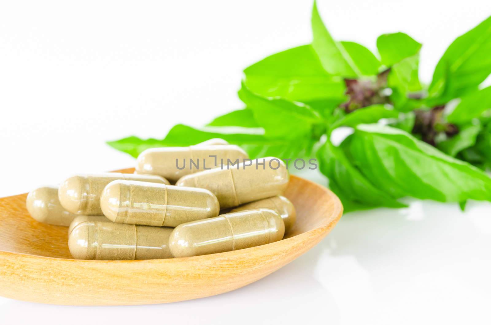 Yellow herbal capsule medicine drug in wooden spoon and green leaf on white background.