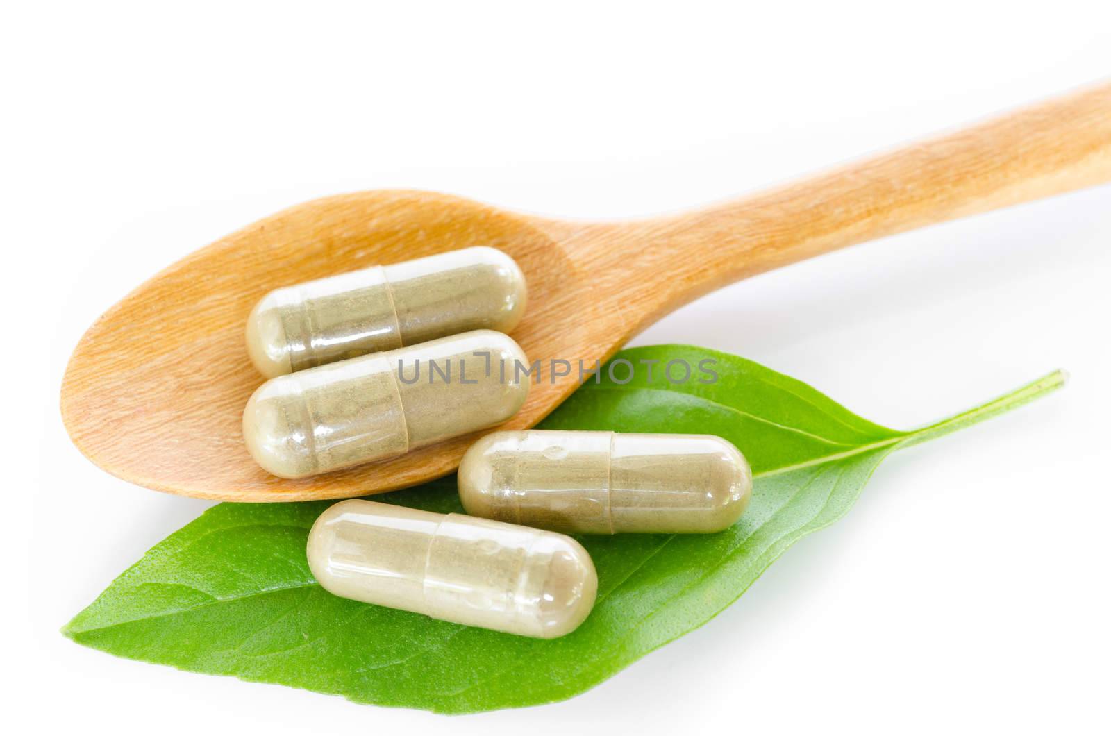 Yellow herb capsule with green leaf in wooden spoon on white background.