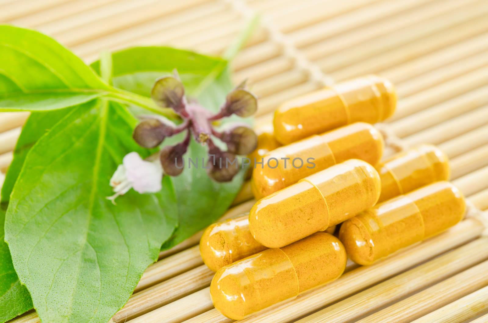 Alternative medicine tablets on a wooden mat, green leaf.