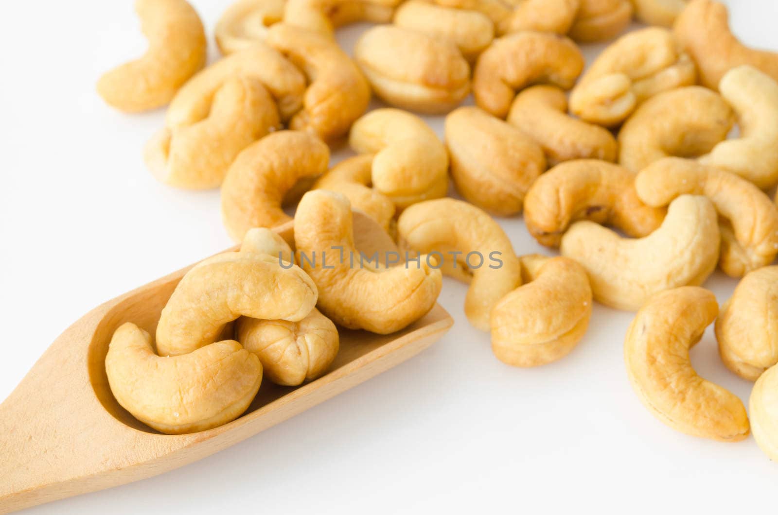 Cashew nuts in wooden spoon on white background.