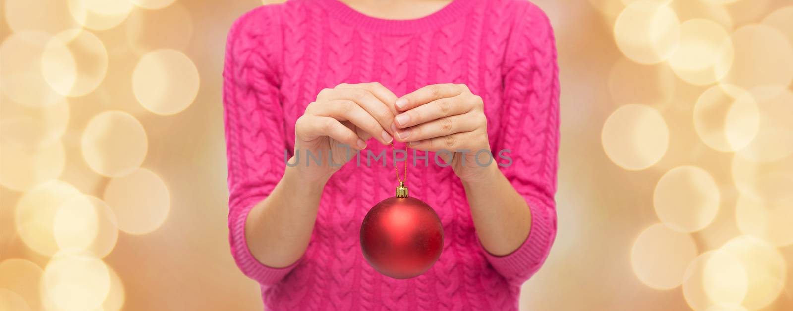 christmas, decoration, holidays and people concept - close up of woman in pink sweater holding christmas ball over beige lights background