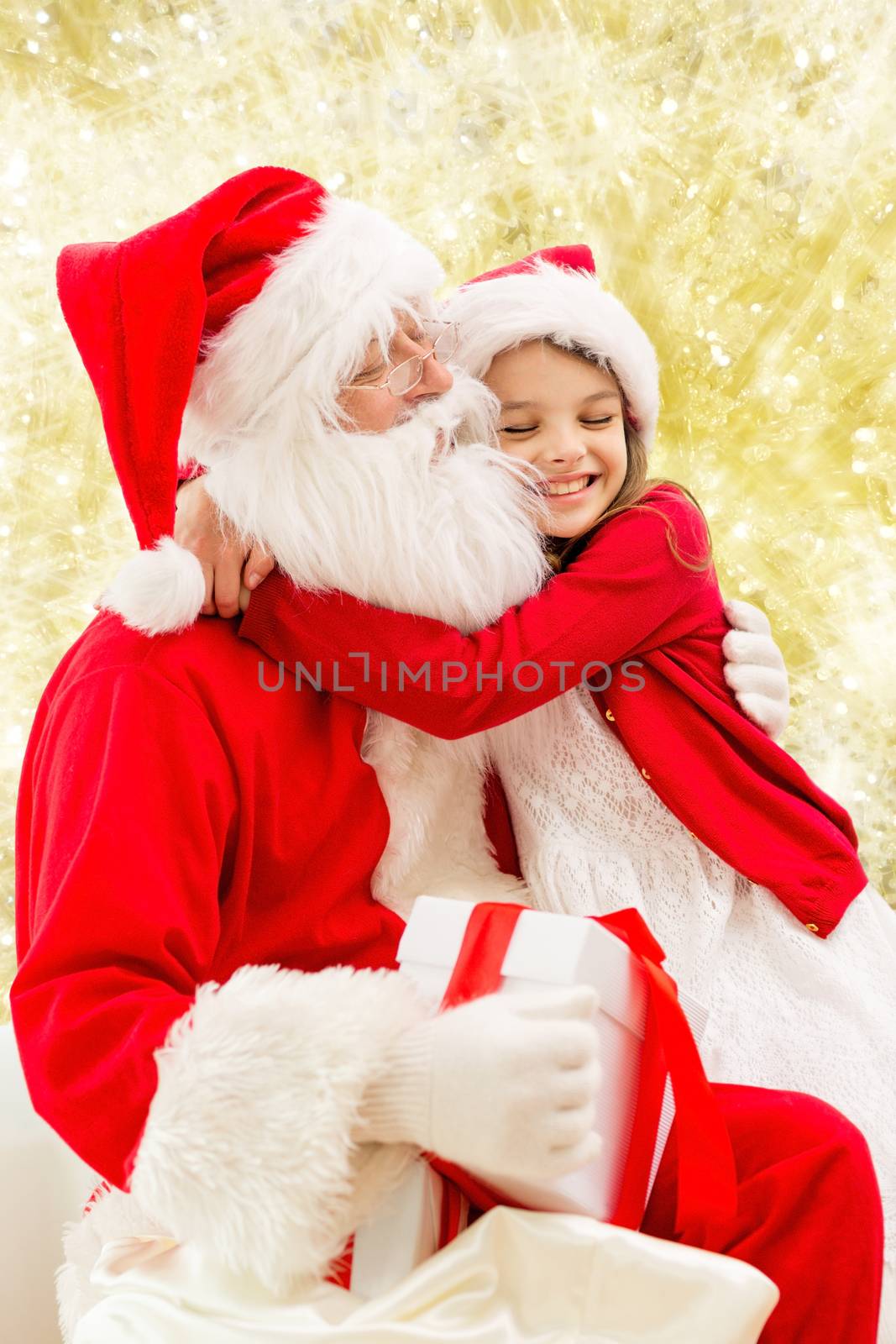 holidays, christmas, childhood and people concept - smiling little girl hugging with santa claus over yellow lights background