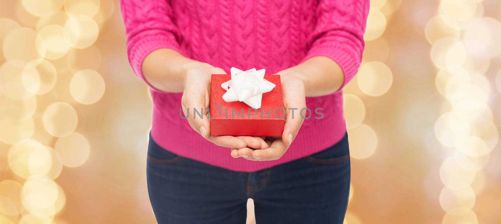 christmas, holidays and people concept - close up of woman in pink sweater holding gift box over beige lights background