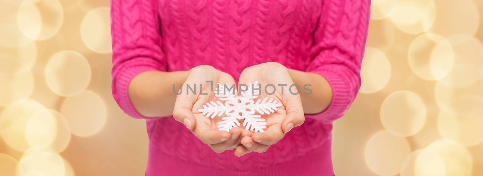 christmas, holidays and people concept - close up of woman in pink sweater holding snowflake over beige lights background