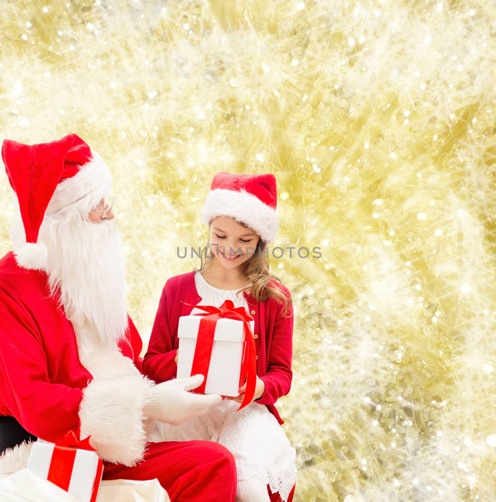 holidays, christmas, childhood and people concept - smiling little girl with santa claus and gifts over yellow lights background