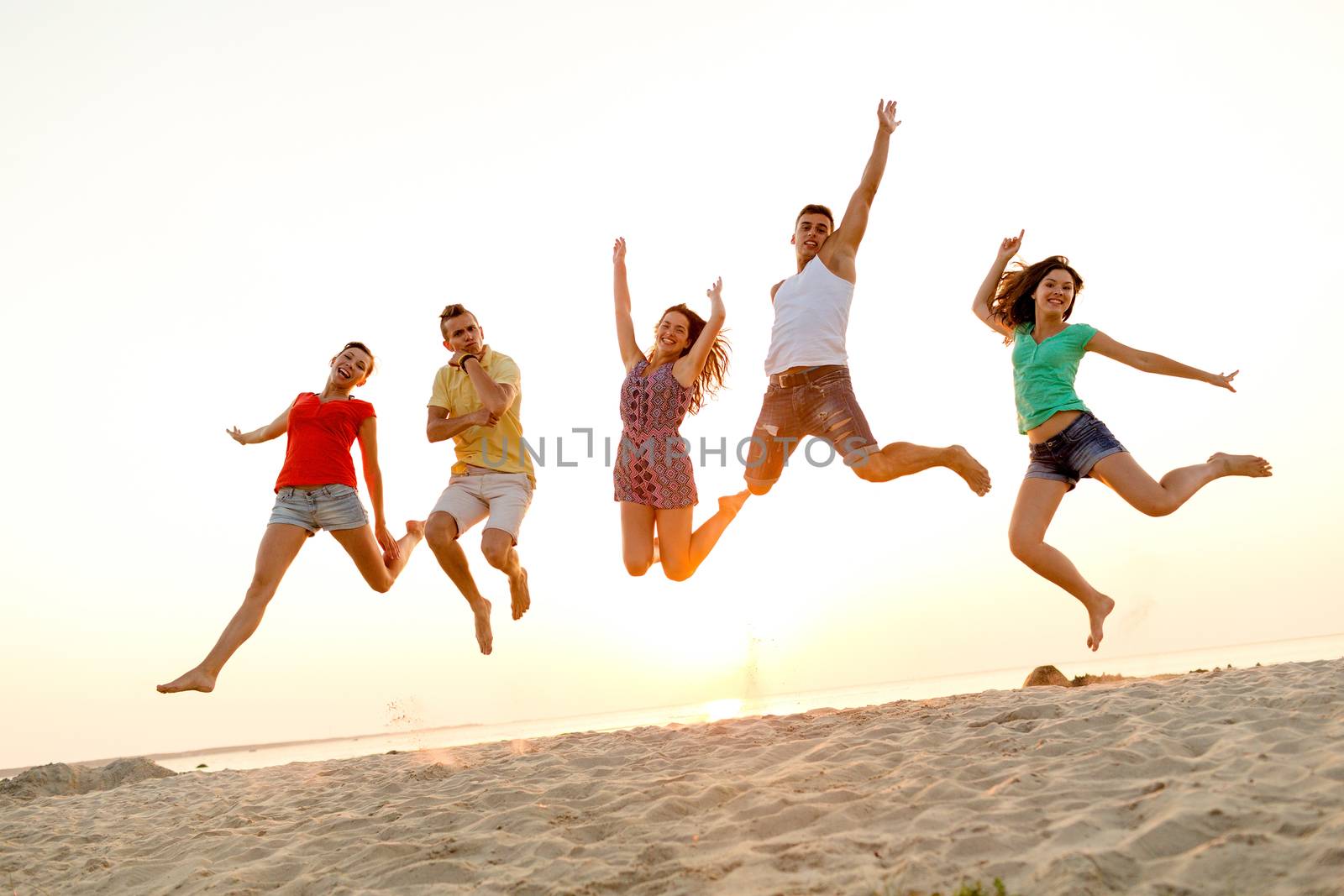 smiling friends dancing and jumping on beach by dolgachov