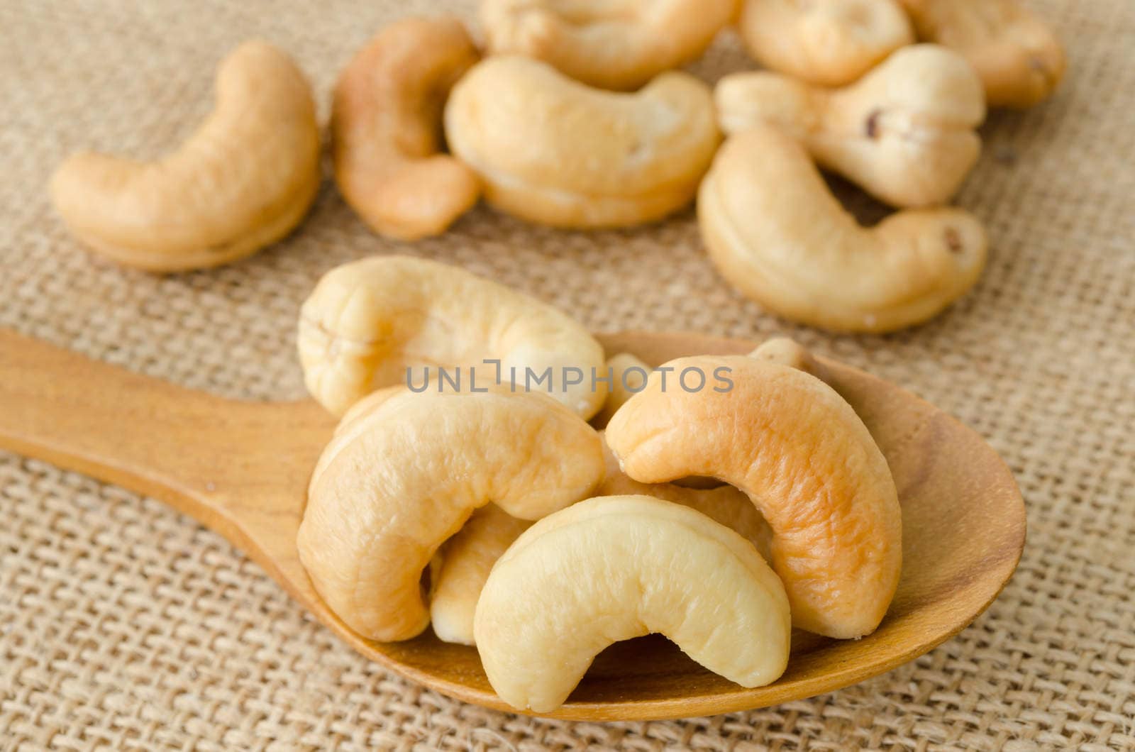 Cashew nuts with salt in wooden spoon on sack background.